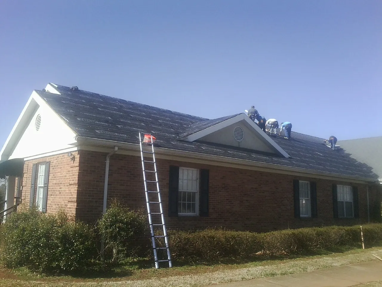 Crew tearing shingles off a brick ranch roof with a ladder set — Emergency Roof Repair work by our crew in Roseville