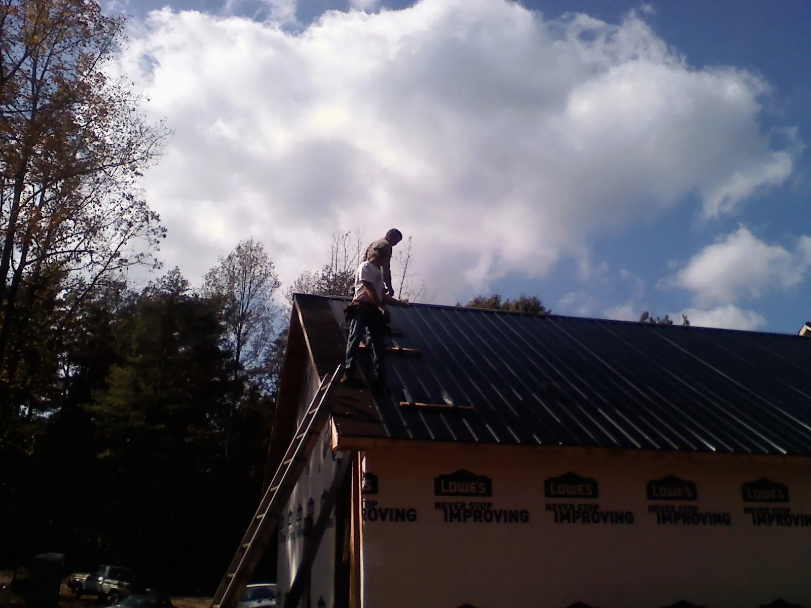 Roofer fastening dark metal panels high against a cloudy sky, from a Roof Inspection job in Roseville